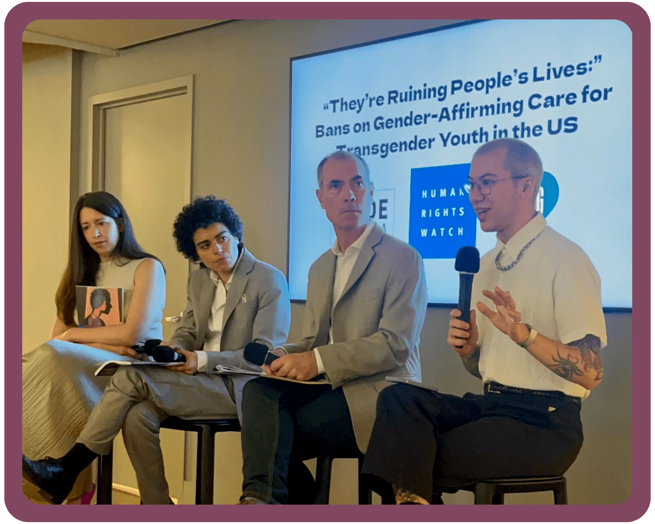 PFLAG NYC Executive Director Clark speaking into a microphone next to three representatives from Human Rights Watch at a press conference for a report release