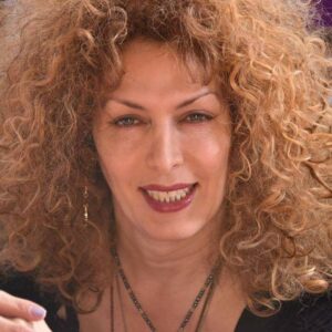 A headshot of Deeangelys Colon, who smiles wearing mauve lipstick and has blonde curly hair.